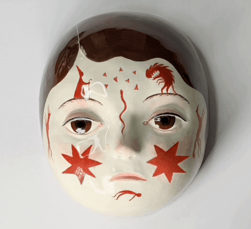 a gif of a ceramic mask with the face of a young girl with red stars and creatures painted on it