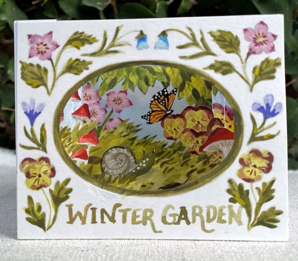 a small paper tunnel book depicting a garden scene, with the words "Winter Garden" written underneath a cutout oval image