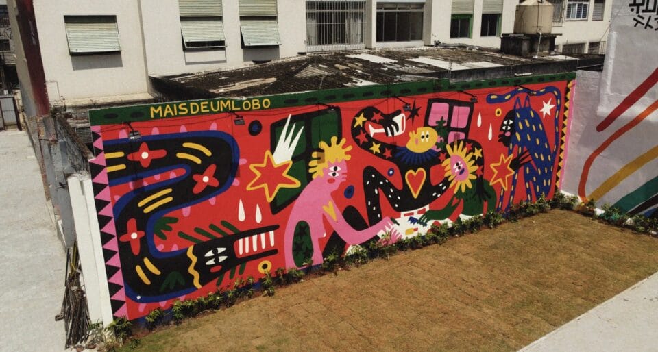 an aerial view of a large mural on the side of a one-story building, depicting cartoonish, fantastical characters drinking and reveling, while a large serpent-like creature approaches from the side